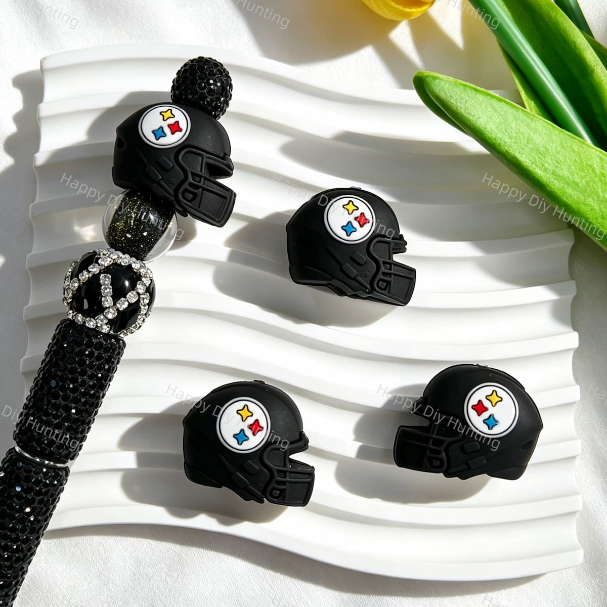 A black 3D football helmet silicone focal bead displayed with a black rhinestone beadable pen. Soft, durable, and flexible, perfect for sports-themed beadable pens, keychains, and handmade crafts.