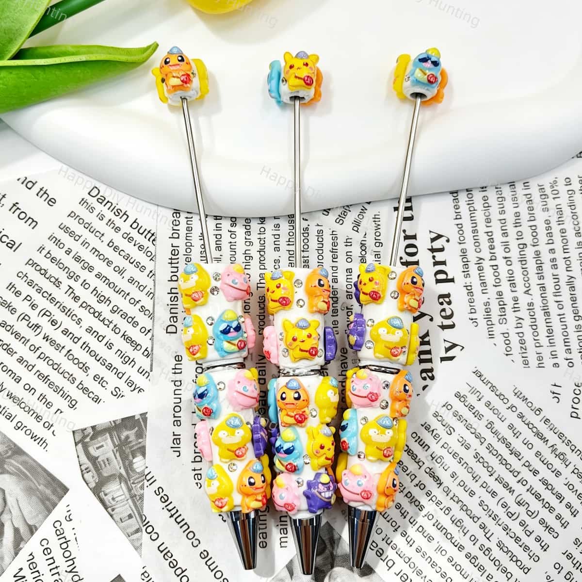 Close-up of four mixed color cartoon monster character beadable pens on a white background. Each pen features white beads decorated with colorful cartoon monster figures and clear rhinestones, paired with silver metal tips. Perfect for DIY crafts, focal beads, and handmade gifts.