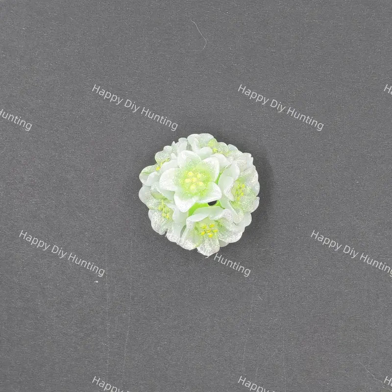 A small white and light green artificial flower craft embellishment, photographed from above on a dark gray textured background with repeating 'Happy DIY Hunting' watermarks.