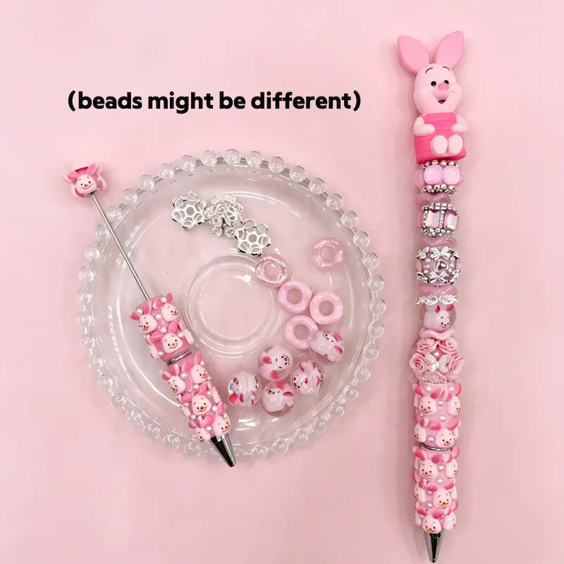 Piglet inspired pink beadable pen set with a cute pink pig cartoon character topper, matching silicone beads, and silver rhinestone spacers.