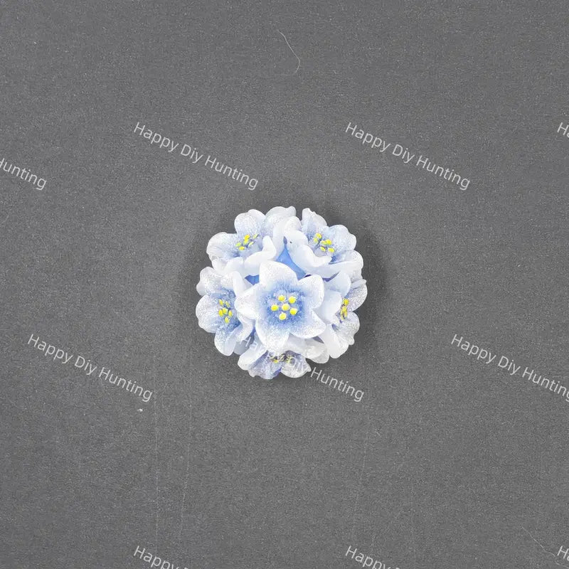 A small cluster of light blue and white faux flowers with yellow centers, arranged in a circular cluster on a dark gray textured background.