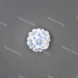 A small cluster of light blue and white faux flowers with yellow centers, arranged in a circular cluster on a dark gray textured background.