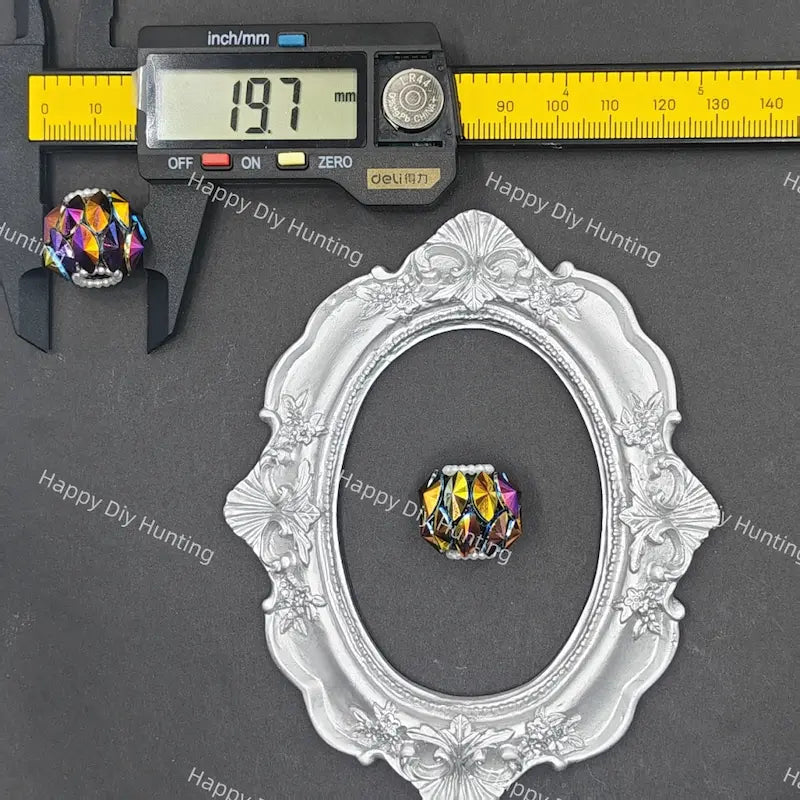 A faceted, iridescent crystal bead shown with a digital caliper reading 19.7 mm and an ornate silver oval frame for scale, on a dark gray background with repeated Happy DIY Hunting watermarks.