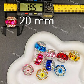 A set of colorful rhinestone-embellished round beads displayed on a white dish, with a digital caliper measuring one pink bead and large overlaid text reading 20 mm.
