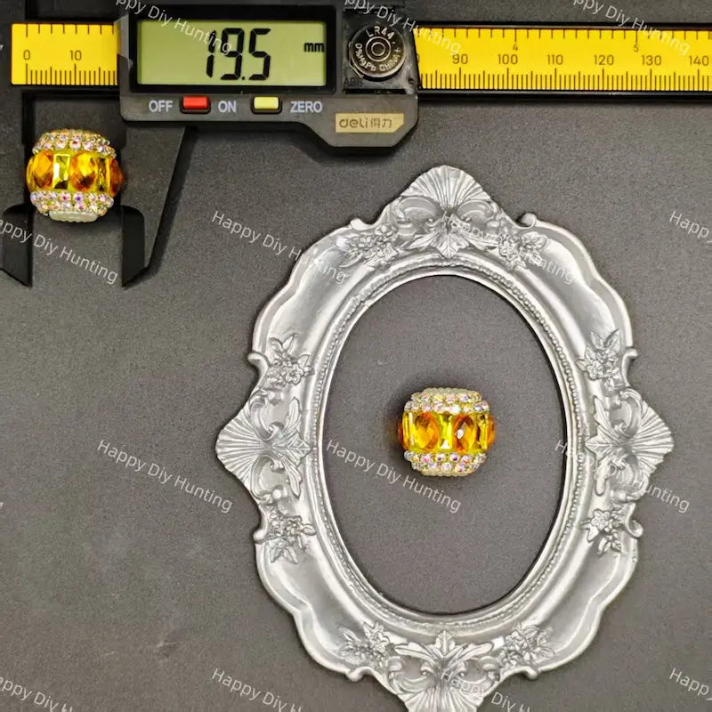 A rectangular yellow crystal bead with a silver-toned border and clear rhinestone accents, displayed on a gray background with a decorative silver frame and a caliper showing 19.5 mm measurement.