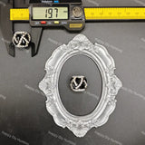 A black and silver interlocking V ring displayed in an ornate silver oval frame, with a digital caliper showing 19.7 mm and a yellow ruler in the background.