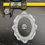 A round cabochon gemstone with blue and clear stones, displayed inside an ornate silver oval frame, with a digital caliper showing 20.0 mm above it on a dark background.