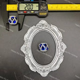 A ring with a blue and white geometric patterned center and clear crystal-like border, displayed on a dark surface with a decorative silver frame and a digital caliper above it for size reference. 