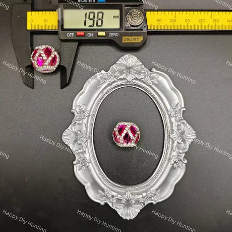 A single round gemstone jewelry piece displayed on a black surface, with a silver ornate frame and a caliper above it showing a 19.8 mm measurement.