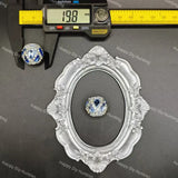 A small round blue and clear rhinestone bead or cabochon displayed on a dark gray surface, with a caliper above it showing 13.8 mm measurements and an ornate silver frame below for scale.