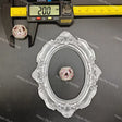 A pink rhinestone cabochon gemstone displayed on a black background, with a silver ornate oval frame and a digital caliper showing 20.0 mm measurements above it.