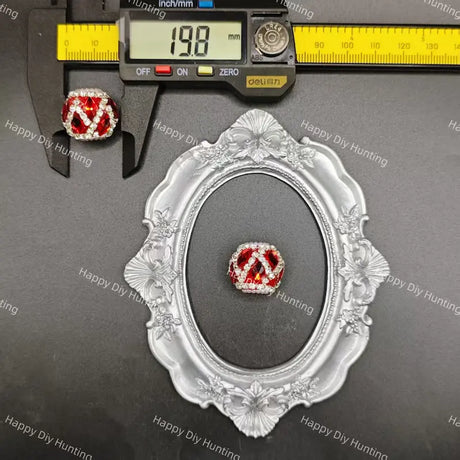 A red and clear gemstone necklace with a large interlocking 'V' design is displayed on a dark gray background, framed by a decorative silver frame. A black caliper at the top shows the necklace's width as 19.