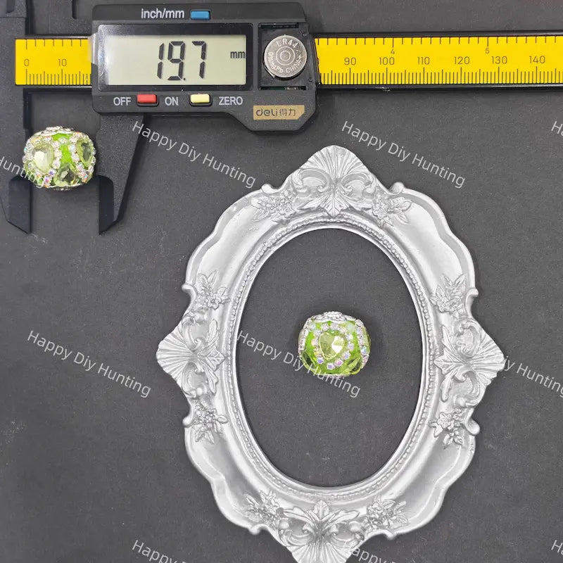 A small oval glass bead with green and white marbled swirls is shown with a silver ornate frame, a caliper, and a digital micrometer on a dark gray background with 'Happy DIY Hunting' watermarks.