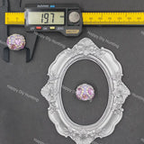 A close-up product photo of an oval, ornate silver frame with a pink and purple floral bead at its center, shown alongside a caliper measuring 19.7 mm and a yellow ruler on a dark gray background.