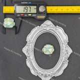 A small iridescent opal-like stone or bead shown with a silver ornate frame, a digital caliper reading 19.7 mm, and a yellow ruler on a dark gray background.
