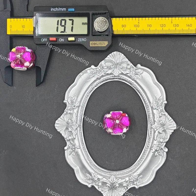 A decorative oval silver frame with floral detailing, shown on a dark gray background with a yellow caliper and a small pink gemstone. The caliper display reads 19.
