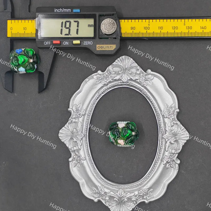 A green and white marbled glass bead is shown inside an ornate silver oval frame, with a caliper measuring the bead on the left and a yellow ruler at the top for scale, all on a dark gray background with Happy Diy Hunting watermarks.