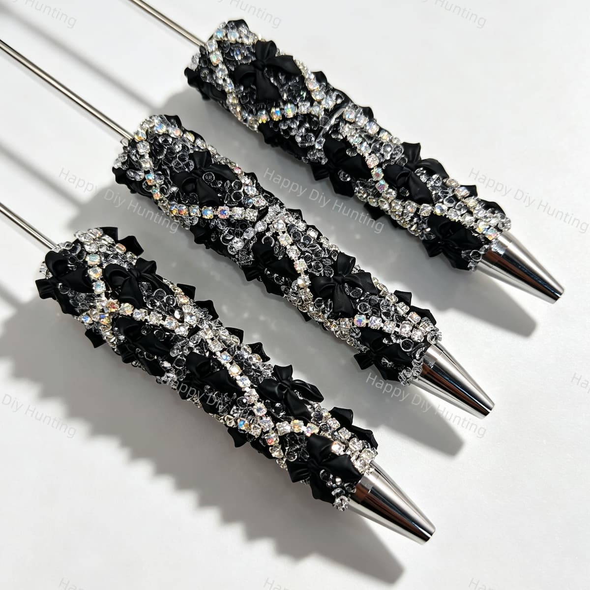 Close-up of three black rhinestone bow beadable pens on a white background. Each pen features a black beaded barrel decorated with sparkling clear rhinestones and black bow accents, paired with silver metal tips. Ideal for DIY beadable pen projects, focal beads, and pen toppers.