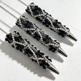 Close-up of three black rhinestone bow beadable pens on a white background. Each pen features a black beaded barrel decorated with sparkling clear rhinestones and black bow accents, paired with silver metal tips. Ideal for DIY beadable pen projects, focal beads, and pen toppers.