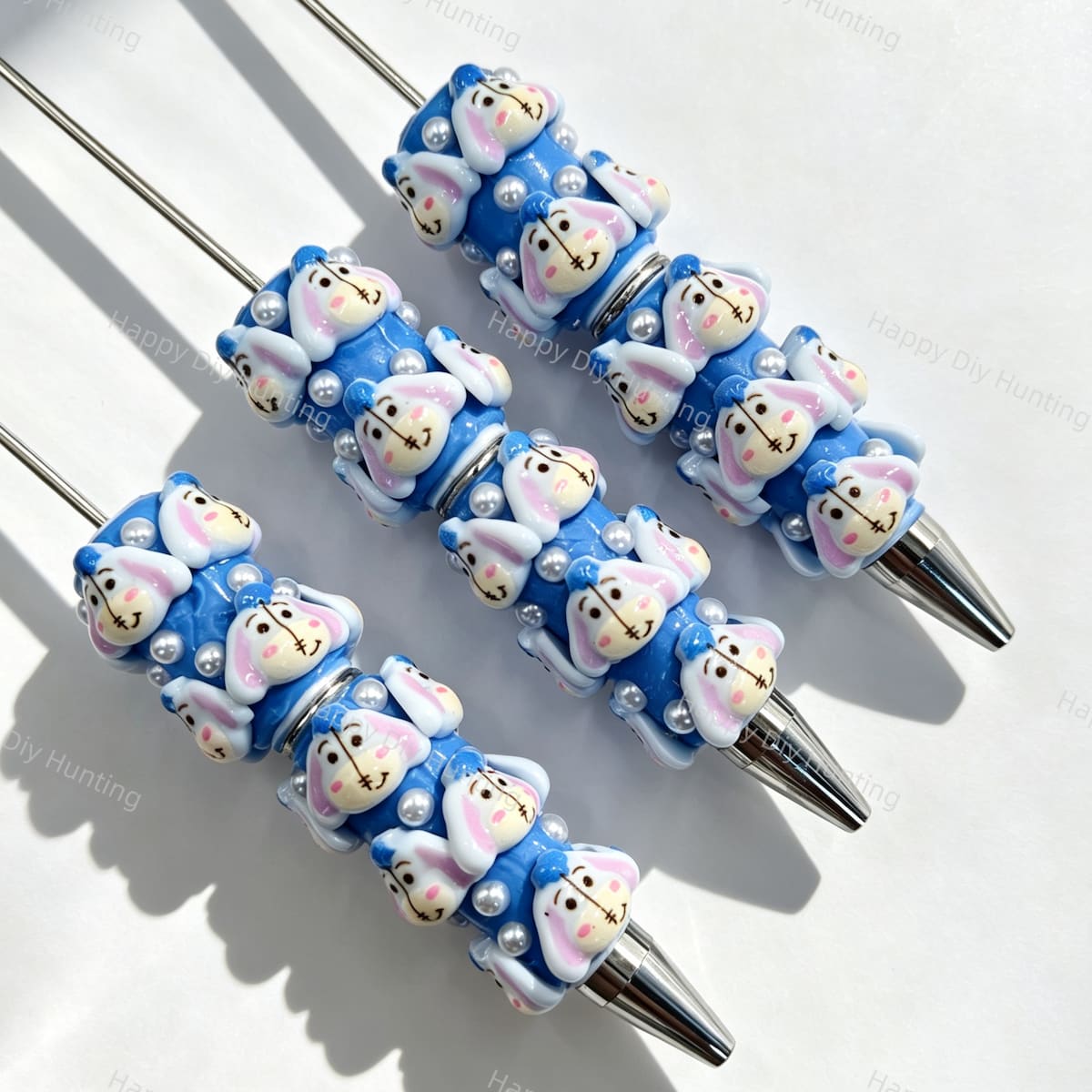 Close-up of four blue bunny cartoon character beadable pens on a white background. Each pen features blue beads decorated with bunny faces and white faux pearls, paired with silver metal tips. Ideal for DIY beadable pen projects, focal beads, and pen toppers.