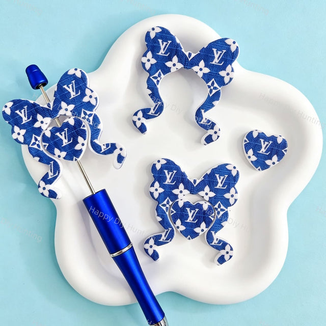 Bow-shaped silicone focal beads featuring a blue fabric texture and V*L monogram pattern design. Soft, durable, and flexible, perfect for beadable pens, keychains, and handmade crafts.