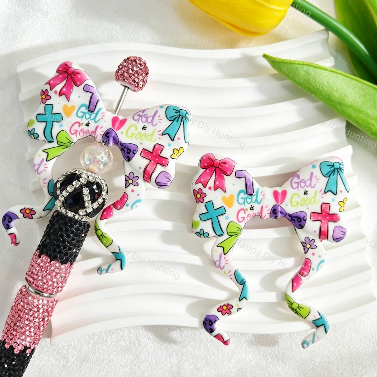 Bow-shaped silicone focal beads featuring a colorful cross and "God is Good" print design. Soft, durable, and flexible, perfect for beadable pens, keychains, and handmade crafts.