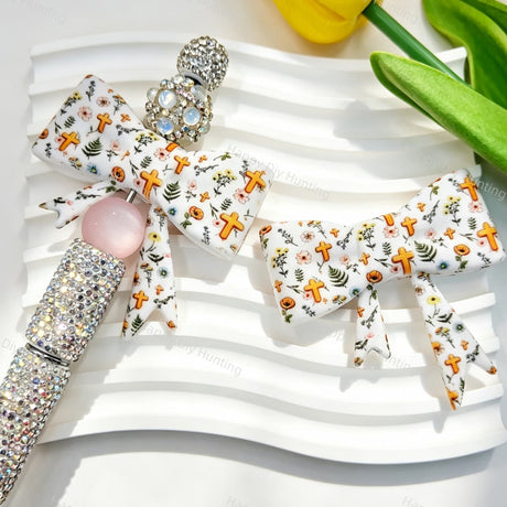 Bow-shaped silicone focal beads featuring a cross and wildflower print design. Soft, durable, and flexible, perfect for beadable pens, keychains, and handmade crafts.
