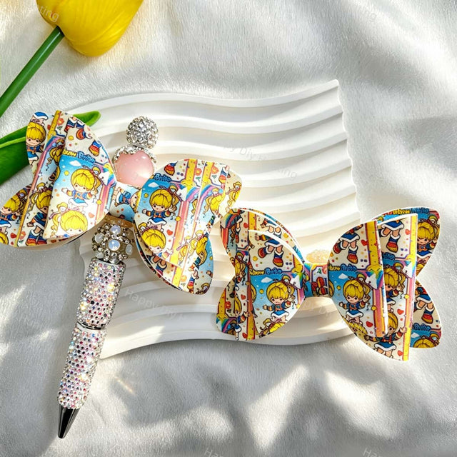 White bow-shaped PU leather focal beads with colorful cartoon girl designs. Shown with a rhinestone beadable pen and a pink round bead. Perfect for beadable pens, keychains, and handmade crafts.