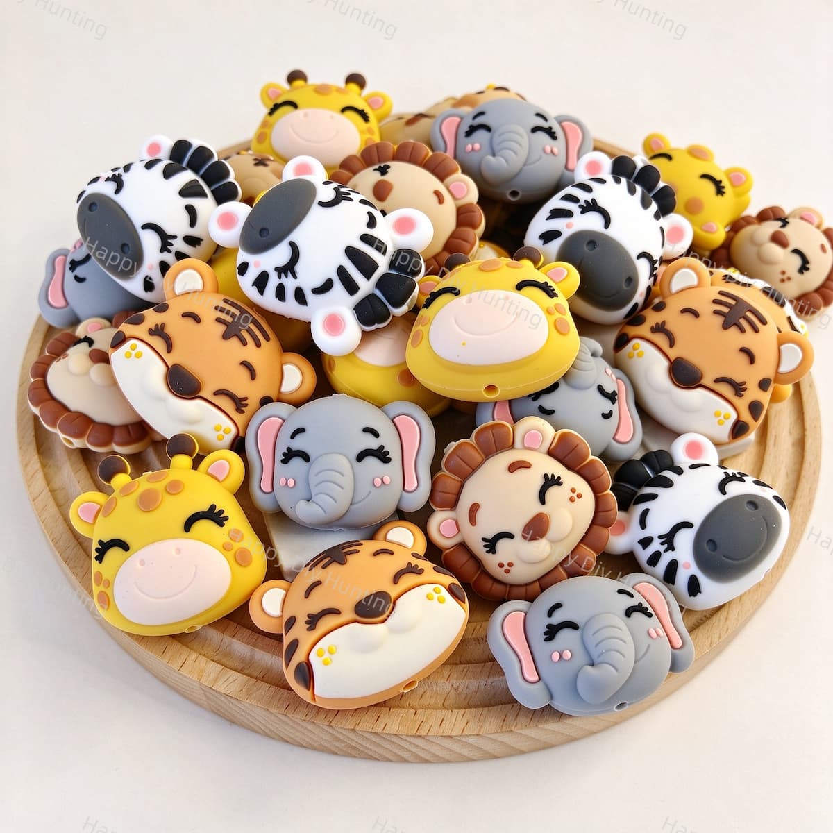 A mixed pile of cute safari animal silicone focal beads on a wooden tray. Designs include tiger, giraffe, lion, zebra, and elephant, all with closed eyes and sweet smiles. Soft, durable, and perfect for beadable pens, keychains, and handmade crafts.