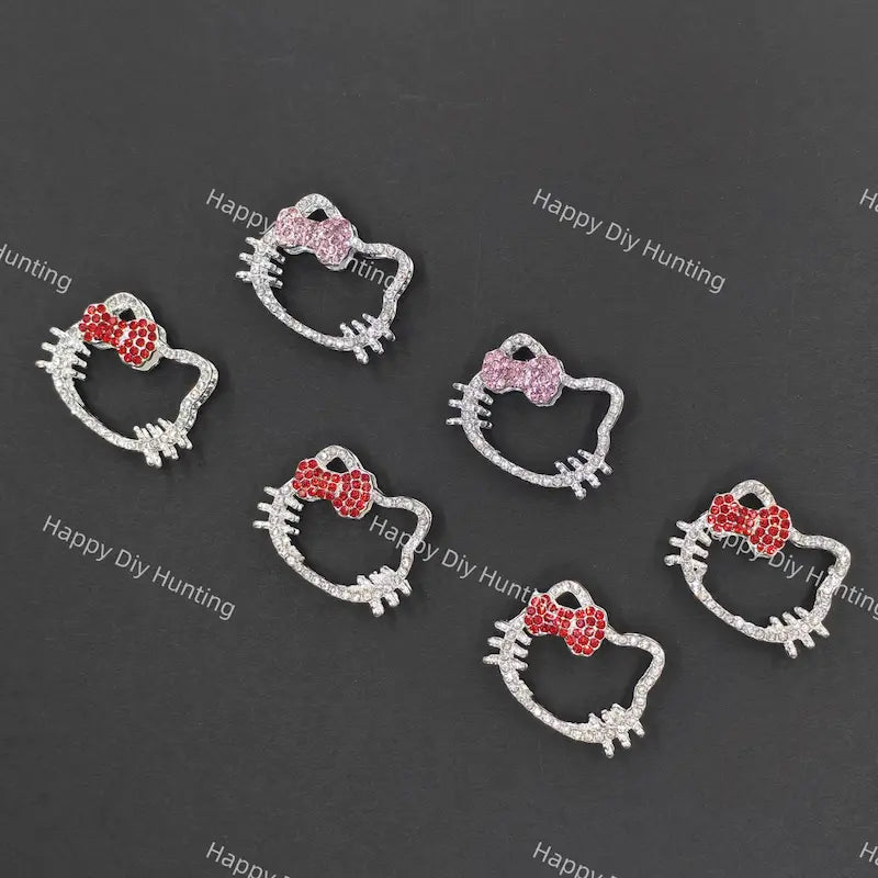 Five silver Hello Kitty face charms with bows, arranged on a dark gray background. Three charms feature red crystal bows, and two feature pink crystal bows.