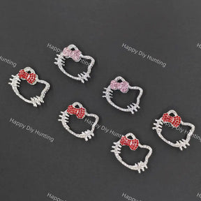Five silver Hello Kitty face charms with bows, arranged on a dark gray background. Three charms feature red crystal bows, and two feature pink crystal bows.