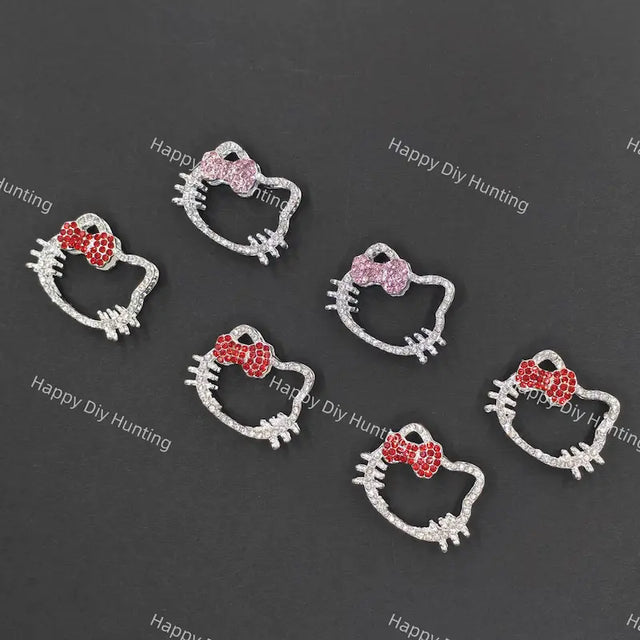 Five silver Hello Kitty face charms with bows, arranged on a dark gray background. Three charms feature red crystal bows, and two feature pink crystal bows.