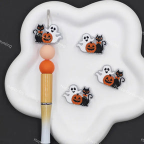 Halloween-themed nail art decals featuring cute cartoon ghosts, black cats, and orange pumpkins, displayed on a white cloud-shaped tray next to a gold and white pen.