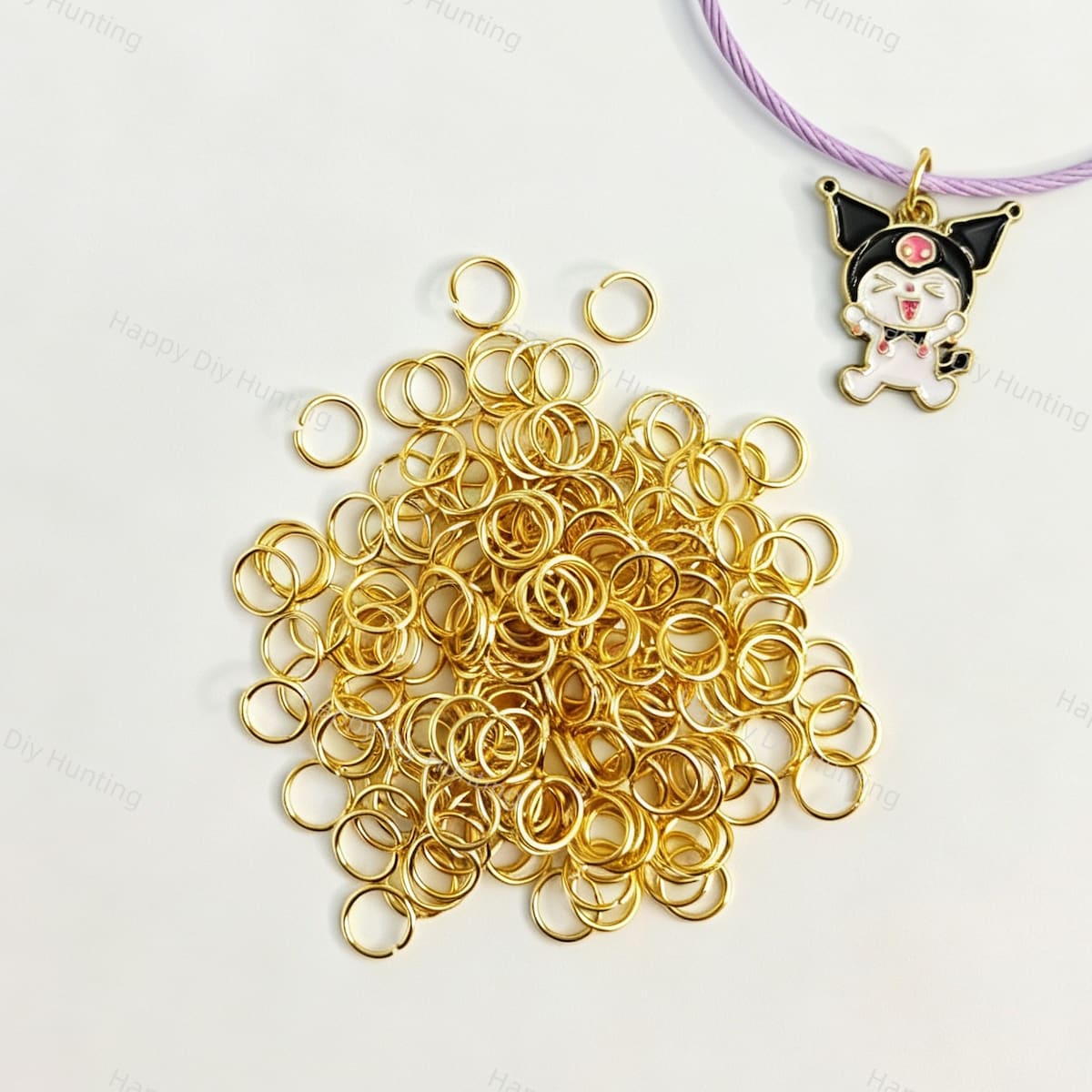 A pile of shiny gold open jump rings for jewelry making and crafts. Shown with a purple cord and a black and white cartoon character charm as a usage example. Perfect for connecting beads, pendants, and keychain charms.