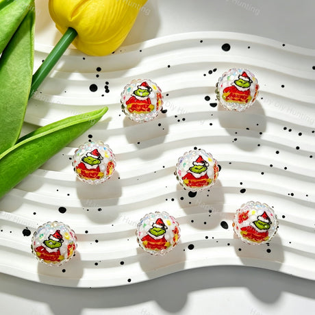 Clear acrylic beads featuring a green cartoon character wearing a Santa hat and red outfit, surrounded by colorful candy dots and a faceted rhinestone surface. Perfect for DIY beadable pens, keychains, and handmade holiday crafts.
