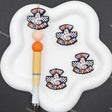Three 'Hippie Happy Halloween' embroidered patches displayed on a white cloud-shaped tray next to a pen, set against a dark gray background with faint watermarks.