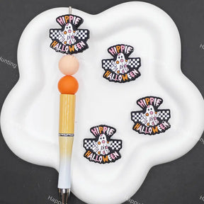 Three 'Hippie Happy Halloween' embroidered patches displayed on a white cloud-shaped tray next to a pen, set against a dark gray background with faint watermarks.