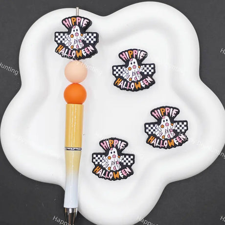 Three 'Hippie Happy Halloween' embroidered patches displayed on a white cloud-shaped tray next to a pen, set against a dark gray background with faint watermarks.