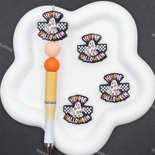 Three 'Hippie Happy Halloween' embroidered patches displayed on a white cloud-shaped tray next to a pen, set against a dark gray background with faint watermarks.