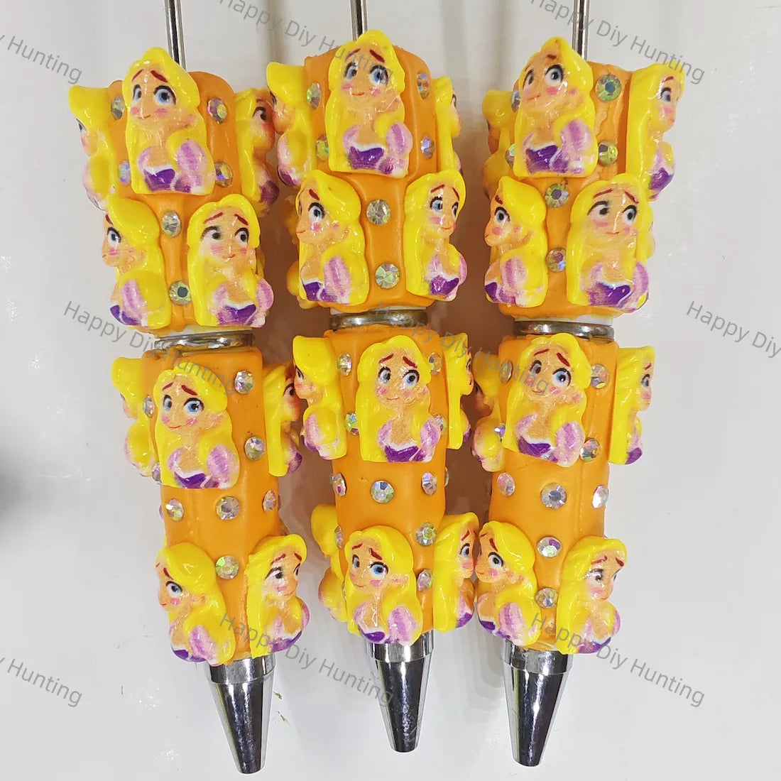 Pre‑assembled beadable pens stacked with long‑blonde‑hair princess figurines. Bright orange base embedded with sparkling rhinestones. Cute themed ballpoint pens for gifts, bulk craft supplies.