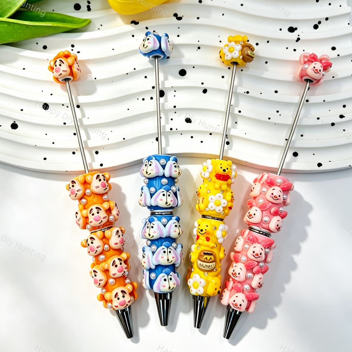 Four mixed cartoon animal character beadable pens displayed on a white wavy tray. Designs include an orange tiger, a blue bunny, a yellow bear with honey and bee details, and a pink pig, each decorated with faux pearls and silver metal tips. Perfect for DIY crafts, focal beads, and handmade gifts.