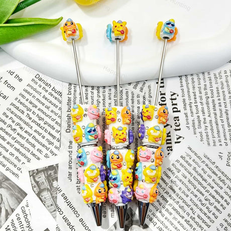 Close-up of four mixed color cartoon monster character beadable pens on a white background. Each pen features white beads decorated with colorful cartoon monster figures and clear rhinestones, paired with silver metal tips. Perfect for DIY crafts, focal beads, and handmade gifts.

