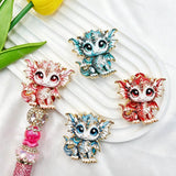Four mixed color cute baby dragon metal fancy beads with rhinestones displayed on a white wavy tray. Colors include blue, red, and white, each featuring a detailed baby dragon with big eyes and rhinestone accents, plus a pink rhinestone beadable pen. Perfect for DIY beadable pens and crafts.