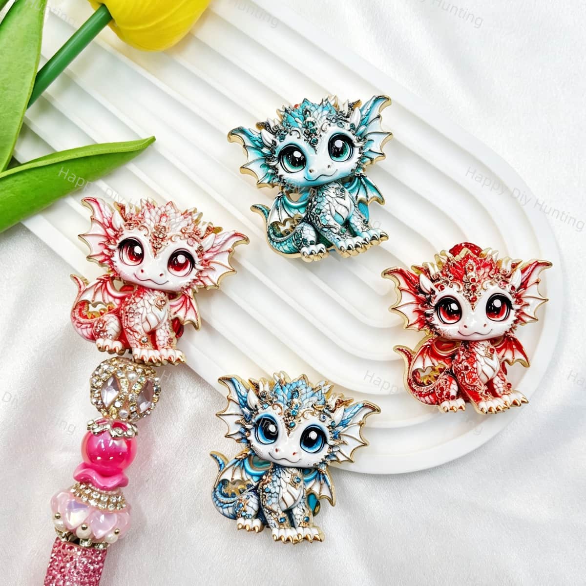 Four mixed color cute baby dragon metal fancy beads with rhinestones displayed on a white wavy tray. Colors include blue, red, and white, each featuring a detailed baby dragon with big eyes and rhinestone accents, plus a pink rhinestone beadable pen. Perfect for DIY beadable pens and crafts.