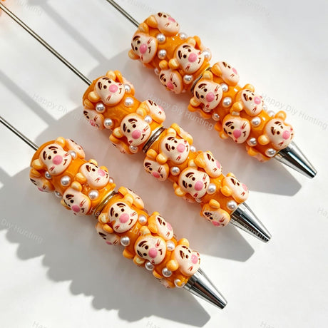 Close-up of four orange tiger cartoon character beadable pens on a white background. Each pen features orange beads decorated with tiger faces and white faux pearls, paired with silver metal tips. Ideal for DIY beadable pen projects, focal beads, and pen toppers.