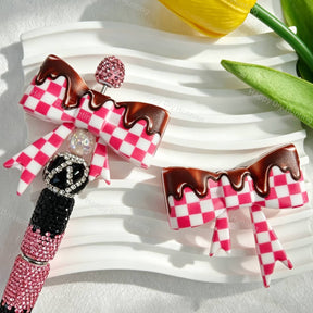 Bow-shaped silicone focal beads featuring a pink checkered pattern with a glossy chocolate drip finish. Soft, durable, and flexible, perfect for beadable pens, keychains, and handmade crafts.