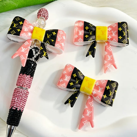 Bow-shaped silicone focal beads featuring a pink and black cute monogram print design. Soft, durable, and flexible, perfect for beadable pens, keychains, and handmade crafts.