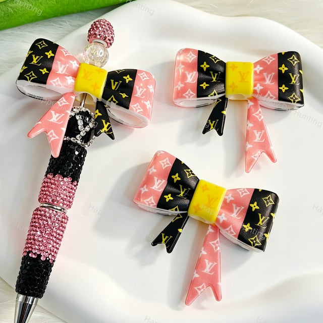 Bow-shaped silicone focal beads featuring a pink and black cute monogram print design. Soft, durable, and flexible, perfect for beadable pens, keychains, and handmade crafts.