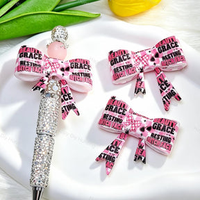 Bow-shaped silicone focal beads featuring a pink and black cute slogan text print design. Soft, durable, and flexible, perfect for beadable pens, keychains, and handmade crafts.