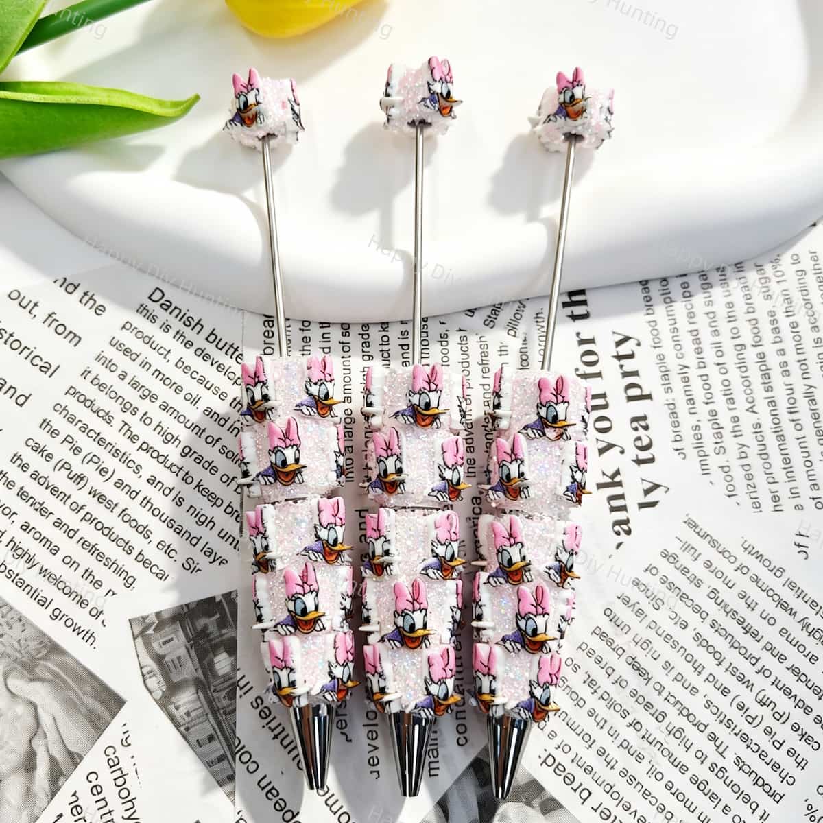 Three pink bow cartoon duck character beadable pens displayed on a newspaper background. Each pen features pink glitter beads decorated with white cartoon duck faces wearing pink bows, plus a silver metal tip. Perfect for DIY crafts, focal beads, and handmade gifts.
